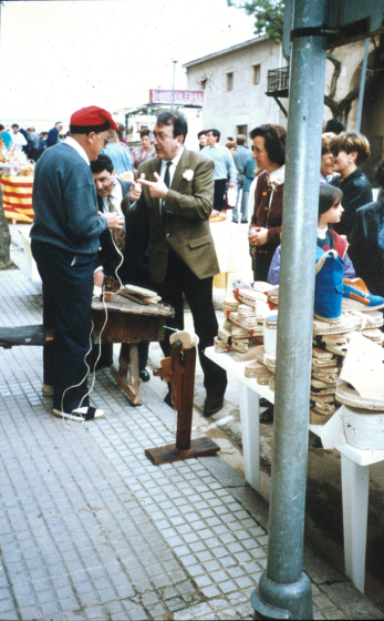 Fira Artesanal de Maçanet pel maig de 1990, el dia de la inauguració.

En Joan Farré delegat de l'autoritat, parlant amb l'artesà espardenyer Agustí Xarbau en presència de Salvadora Roda, una de les persones col·laboradores en l'organització de la fira.