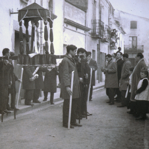 Diada de Sant Sebastià. Després de l'ofici amb orquesta a la capella surt la processó al carrer. Es poden veure el rector Mn Francesc Berga i els escolans Simó Serra i Jaume Costa. Al fons del carrer es veu l'antiga casa Can Palmada, avui desapareguda per donar pas al carrer Salvador Espriu