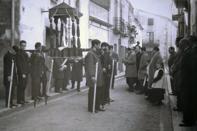 Diada de Sant Sebastià. Després de l'ofici amb orquesta a la capella surt la processó al carrer. Es poden veure el rector Mn Francesc Berga i els escolans Simó Serra i Jaume Costa. Al fons del carrer es veu l'antiga casa Can Palmada, avui desapareguda per donar pas al carrer Salvador Espriu