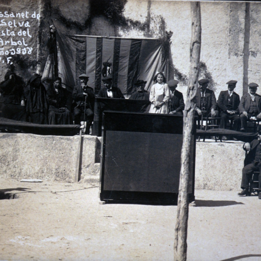 Festa de l'arbre de l'any 1918 a la plaça de l'Església. La presidència de l'acte.

Es poden observar com dos nois planten un arbre mentre una alumna pronuncia un discurs alegoril a l'acte.