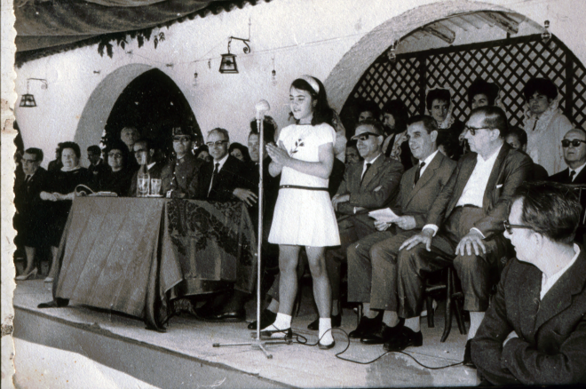 Presidència de la Festa: Joan Viader, Felicitat Llirinós, Angela Reyner, Germiniano Lozar, Antonio Sanz (cap de la guàrdia civil), Bartomeu Comas (delegat de la Caixa), Mn Francesc Berga (rector), un representant de la Caixa, el Sr. Serra (mestre), el Sr. Marsá i Miquel Coll. La nena és Margarita Baltrons recitant una poesia.