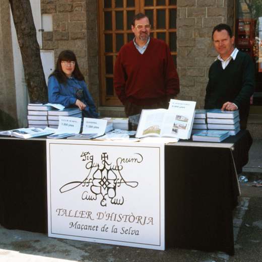 En Lluís Soler i en Narcís Vilella amb una ajudant a la parada de venda de llibres del taller d'història a la fira artesanal de Maçanet