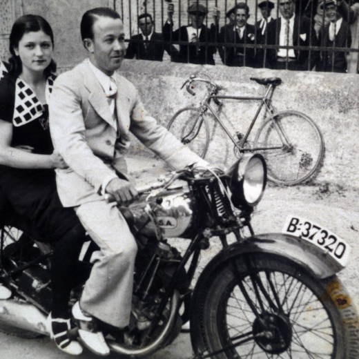 En Francesc Miquel, més conegut com a Paco de Cartellà, posseidor d'una moto marca BSA de les poques que hi havia per aquells anys; amb les germanes Lola i Felicia Pascual de Can Tomàs, en una foto feta davant del local de la Societat Recreativa amb la reixa de Can Falló com a fons.