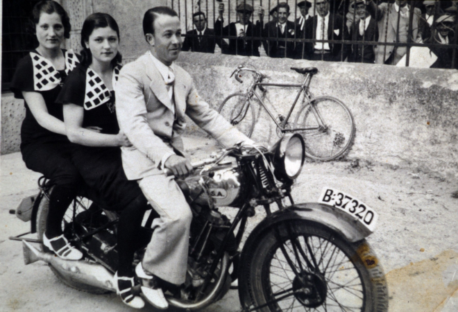 En Francesc Miquel, més conegut com a Paco de Cartellà, posseidor d'una moto marca BSA de les poques que hi havia per aquells anys; amb les germanes Lola i Felicia Pascual de Can Tomàs, en una foto feta davant del local de la Societat Recreativa amb la reixa de Can Falló com a fons.