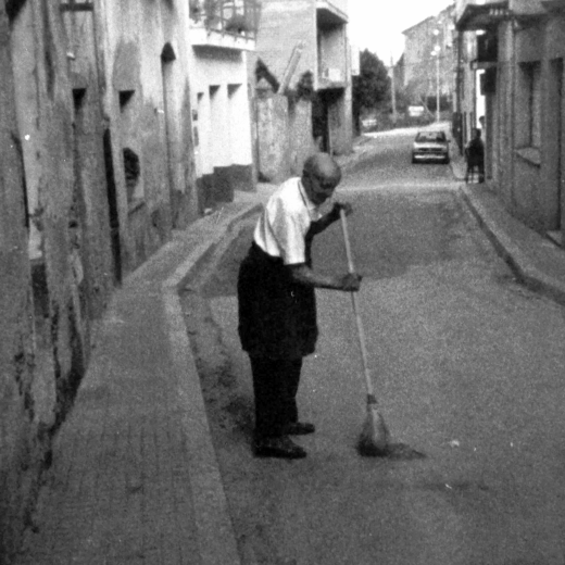 En Lluís Ruhí, barber, escombrant el carrer migdia davant del seu establiment.