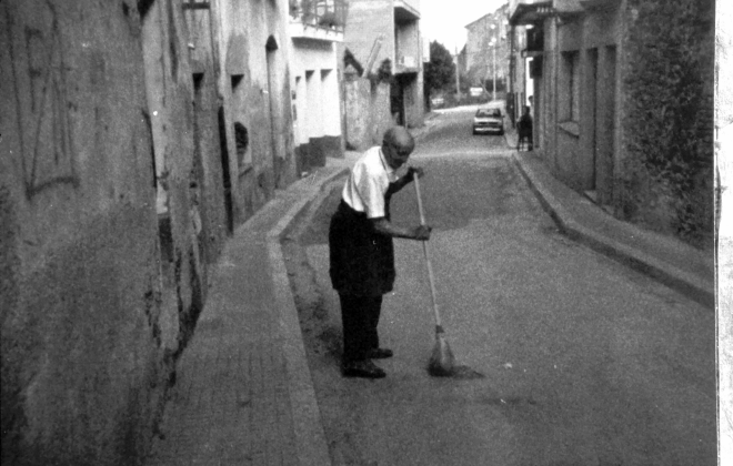 En Lluís Ruhí, barber, escombrant el carrer migdia davant del seu establiment.