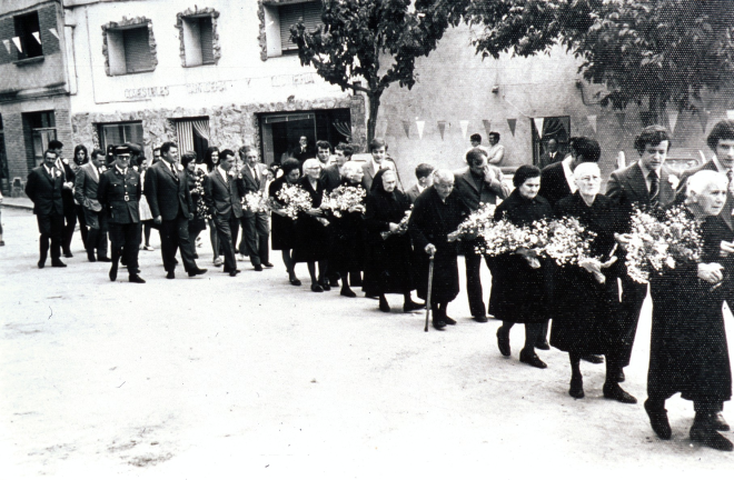 Festa d'homenatge a la vellesa. La comitiva d'homenatjats amb les autoritats dirigint-se cap a l'Església. La primera de la fila és la Dolors Surós amb Jaume Fors; seguidament Carme Tarres i ?; Adela Rossell amb Narcís Selva; Rita Gironés i ?; Dolors Tarres amb el seu nét Joaquim Reyner i finalment, la Dolors Deulofeu.