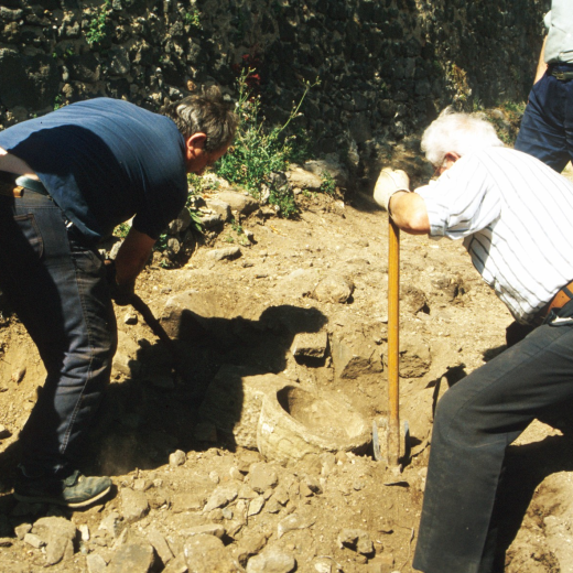 Moment en que és acabada de desenterrar i recuperar la pica de l'aigua beneida de la capella de Sant Jordi, desprès d'haver estat 150 ó 200 anys enderrocada amb més de 2 metres de terra i pedres a sobre. Immediatament fou restaurada i col·locada al seu lloc primitiu a l'entrada de la capella.

A la foto en Josep Panosa i en Martí Tomàs l'acaben de desenterrar en presència de Josep Reyner i Jordi Vergés mentre Juli Campeny feia la foto.
