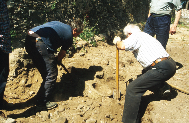 Moment en que és acabada de desenterrar i recuperar la pica de l'aigua beneida de la capella de Sant Jordi, desprès d'haver estat 150 ó 200 anys enderrocada amb més de 2 metres de terra i pedres a sobre. Immediatament fou restaurada i col·locada al seu lloc primitiu a l'entrada de la capella.

A la foto en Josep Panosa i en Martí Tomàs l'acaben de desenterrar en presència de Josep Reyner i Jordi Vergés mentre Juli Campeny feia la foto.