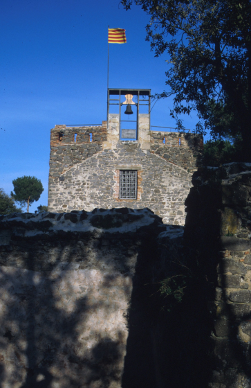 Vista de la façana principal de la Capella de Sant Jordi ja restaurada i amb la campana col·locada al nou campanar. La senyera de Catalunya presideix de dia i nit tot aquest entorn. Els veins de les cases de pagès properes es fixen amb la senyera per saber d'on bé el vent. Aquell dia tirava de tramontana.