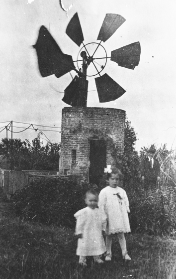 Els germans Joan i Aurelia Lluís Tomàs i al fons el seu pare en Josep Lluís, junt al molí de vent que per aquells temps hi havia a la masia Can Cartellà Nou, casa situada al peu de la carretera Nacional II