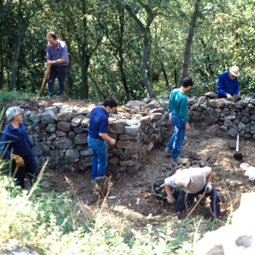 La gent del Taller d'Història treballant en la neteja i desenrunament dels fossars que envolten el recinte, treball previ a la reconstrucció dels murs. En Xavier Vergès, en Josep Panosa, en Francesc Guinart, en Martí Tomàs, en Jordi Vergès, i el que porta barret és en Josep Reyner.