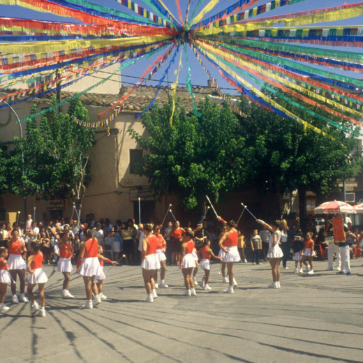 Detall de la plaça de l'església al dia de festa major, amb l'exhibició de les majorets de Maçanet. La plaça està emplenada.
