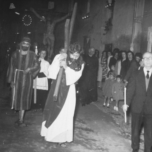Processó del Divendres Sant a Maçanet. Pas de Jesús arrossegant la Creu i en Miquel Coll, un dels organitzadors de la processó, amb un ciri passant pel carrer Migdia.