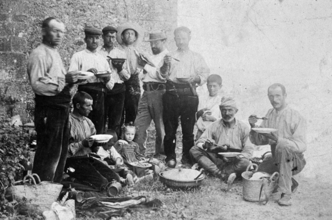 Una colla de treballadors d'en Trinxeria en ple dinar mentre l'amo vigila i llegeix el diari.